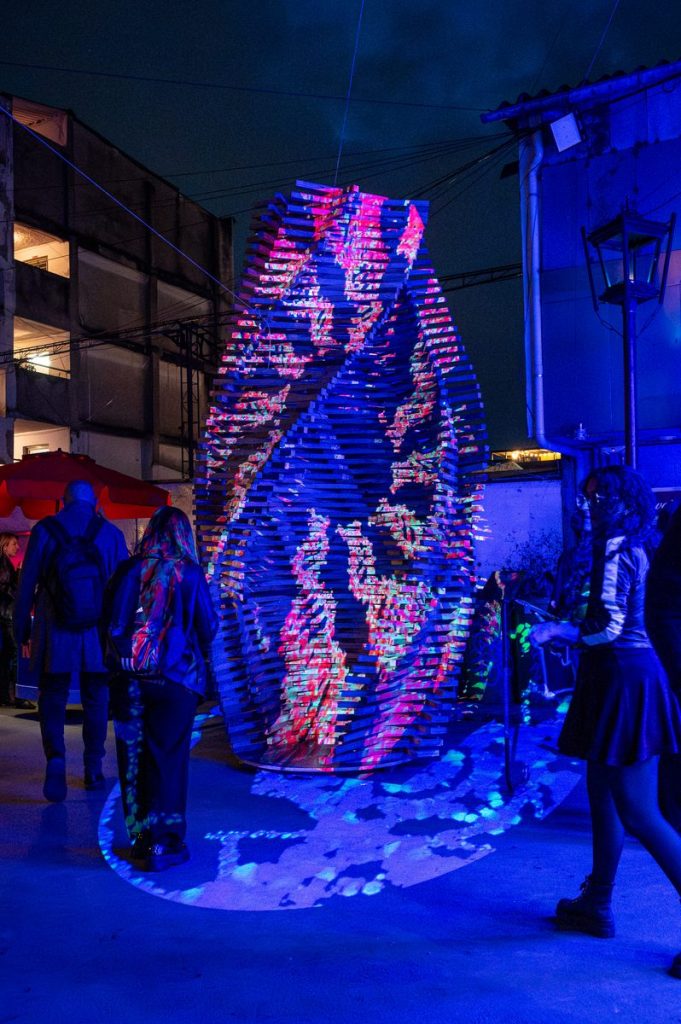 Escultura de madera con proyección mapping en colores azul y rosa